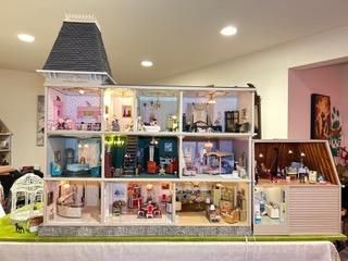 Miniature dollhouse display with lit rooms, tiny furniture, and a chimney on a table in a bright room