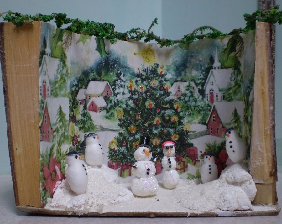 Miniature winter village with snowmen, a decorated Christmas tree, and snowy houses under greenery