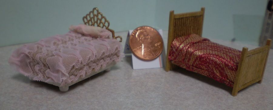 Two miniature beds with pink and red patterned blankets beside a copper tray on a tabletop