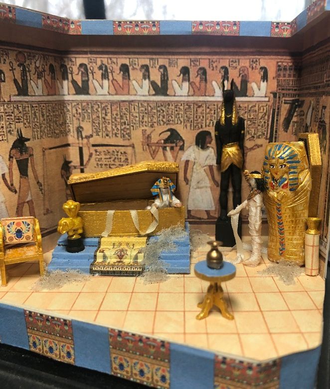 Egyptian tomb diorama with gold sarcophagus, statues, wall paintings, and a person standing inside