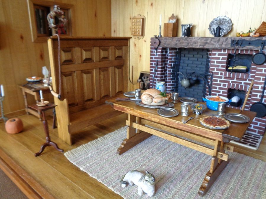 Miniature dining room with wooden table, bench, fireplace, and rug on a wood floor