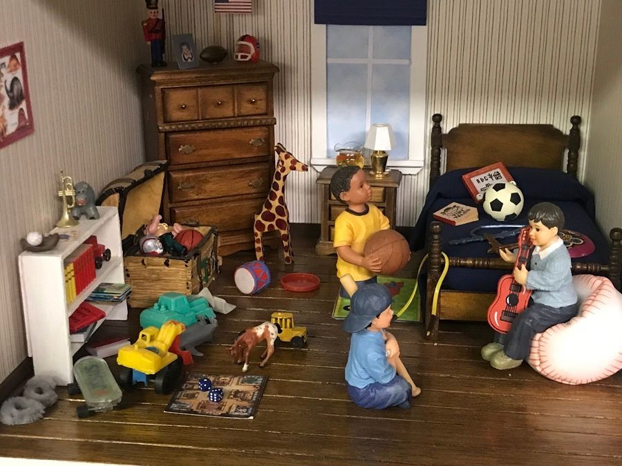 Toy dolls and stuffed animals arranged in a dollhouse bedroom with beds, dresser, and scattered toys.