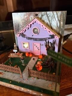 Miniature Halloween house display with pink trim, pumpkins, spiderwebs, and a fenced yard at dusk