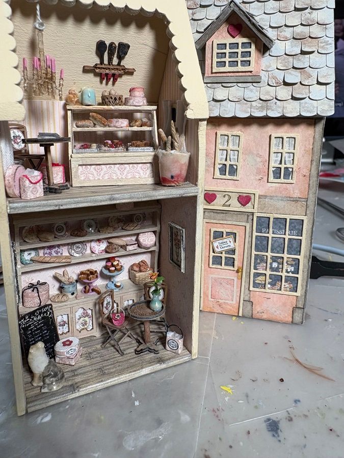 Miniature dollhouse shop and adjoining pastel townhouse with tiny shelves, windows, and heart details.