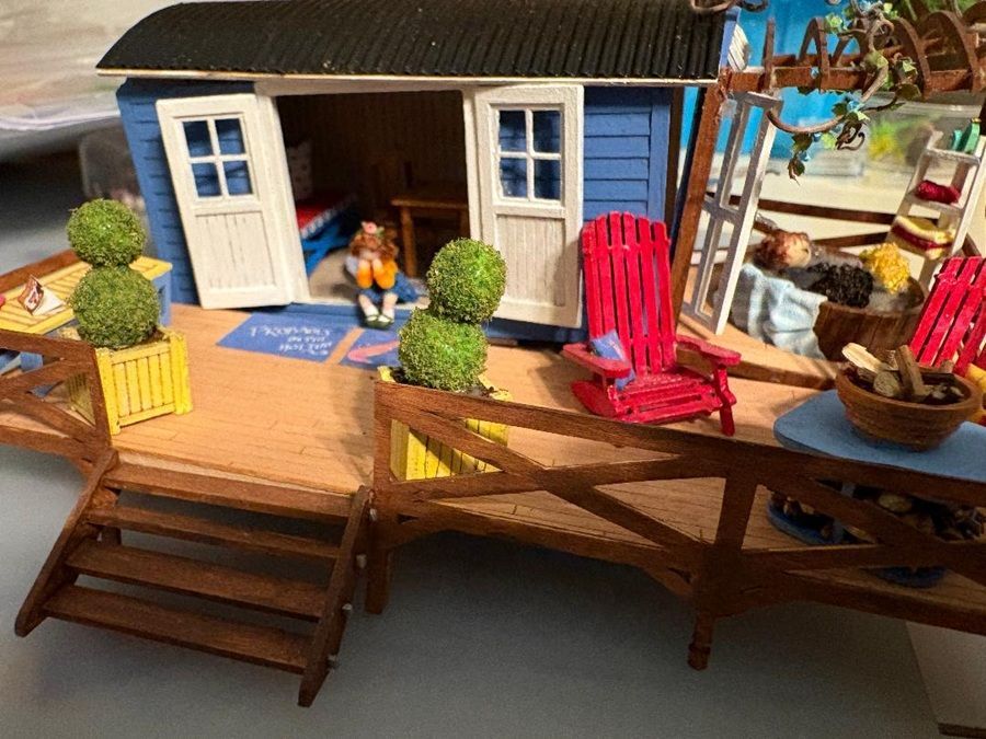 Miniature blue beach cottage porch with red chair, potted plants, and small steps in sunlight