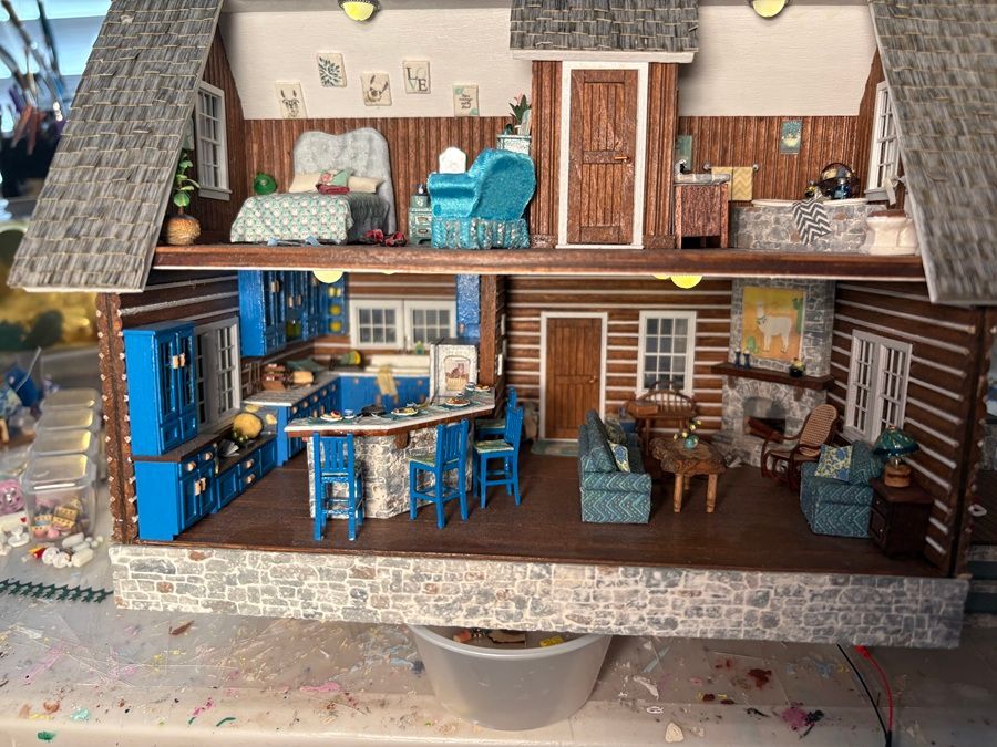 Dollhouse interior with blue kitchen and living room furniture, wood-paneled walls, and a small dining area