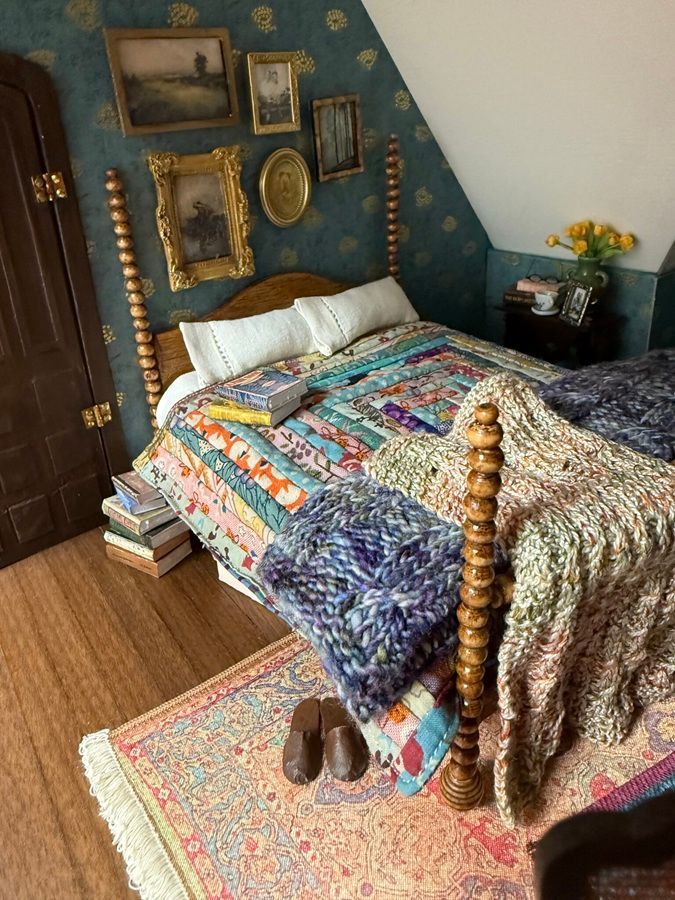 Cozy bedroom with a colorful quilted bedspread, wooden bed frame, framed wall art, and a small side table with flowers