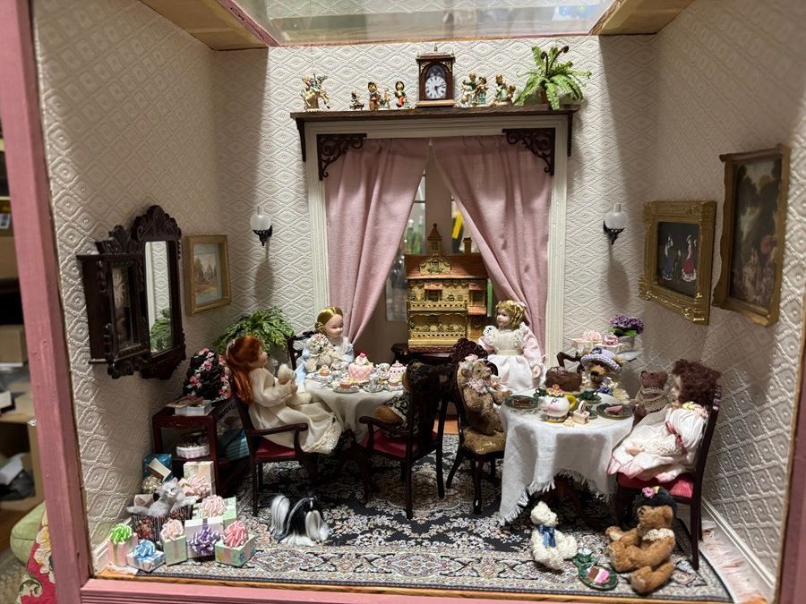 Miniature dining room diorama with a table set for tea, pink curtains, and decorative furniture and plants.