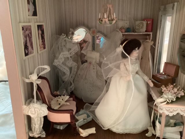 Three dolls in white dresses posed in a vintage dollhouse room with floral decor