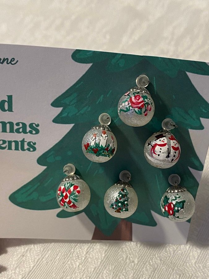 Clear plastic ornament ornaments decorated as Christmas trees hanging on a green paper tree craft display.
