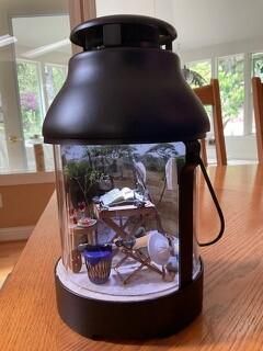 Black lantern-shaped display case with a winter village scene inside on a wooden table.