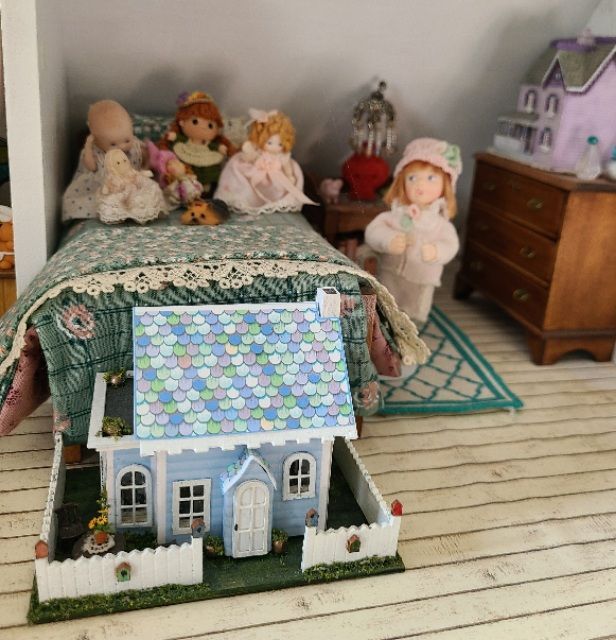 Miniature dollhouse and dolls in a cozy room, with a blue-roofed house in the foreground.