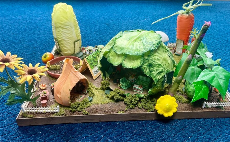 Colorful miniature garden diorama with flowers, leafy plants, and small vegetables on a tray