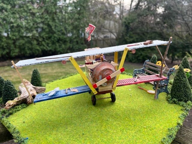 Model biplane on bright green grass with trees in the background, viewed from the front