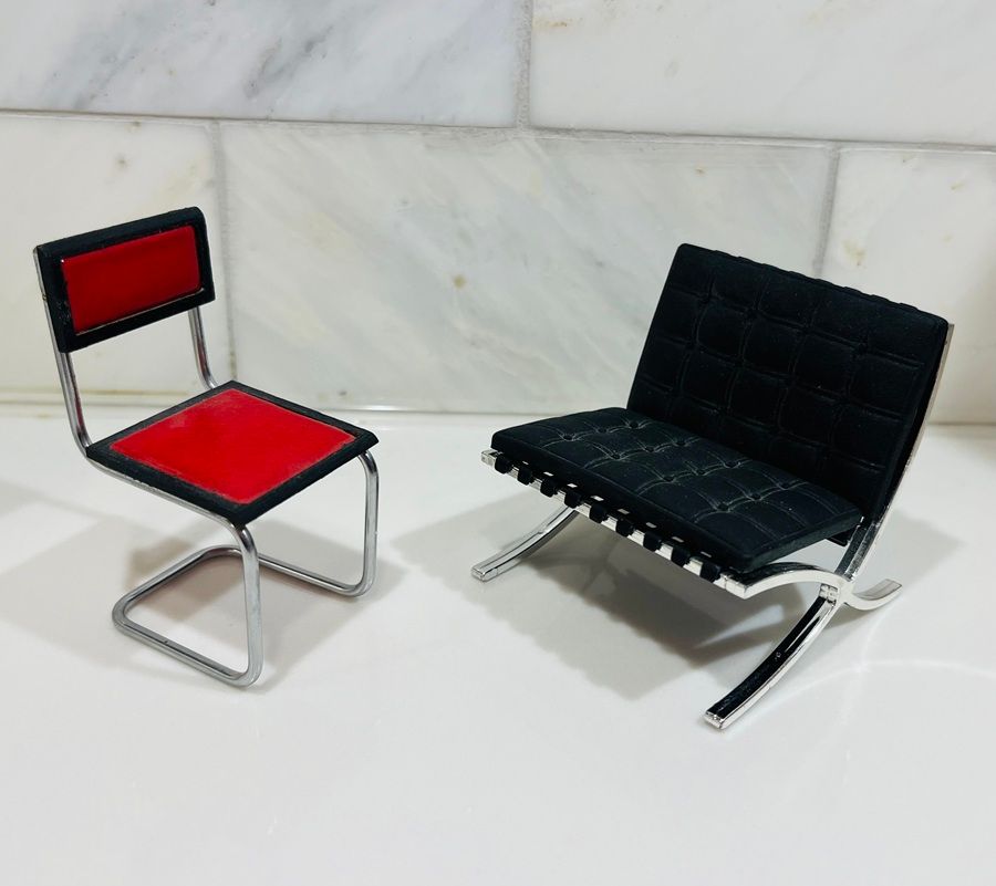 Two modern chairs on a white surface, one red and silver, one black and silver.