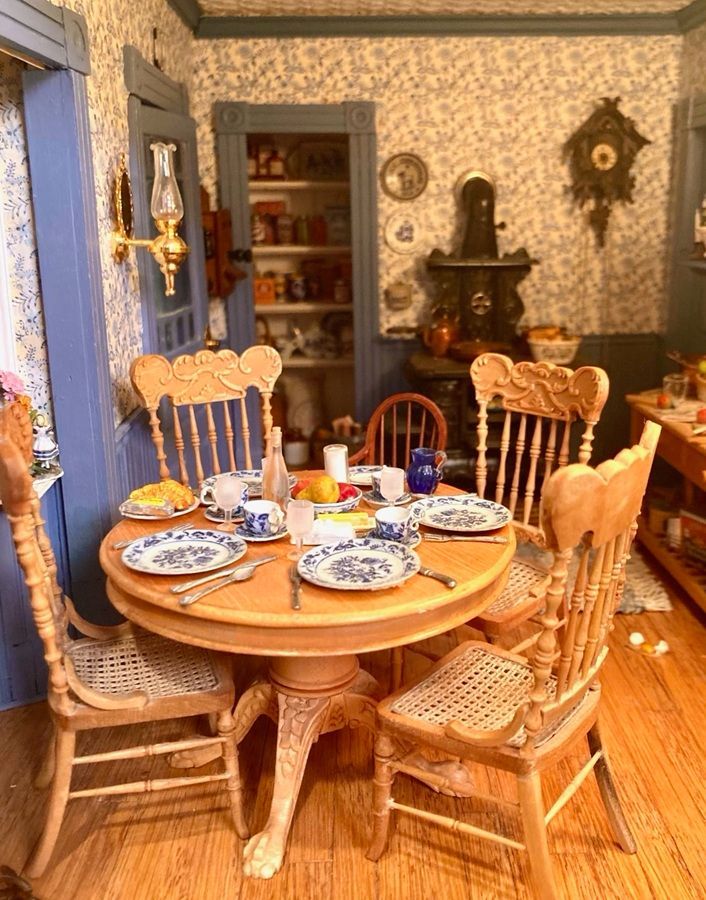 Cozy dining room with round wooden table, four cane chairs, set tableware, and a small fireplace in back.