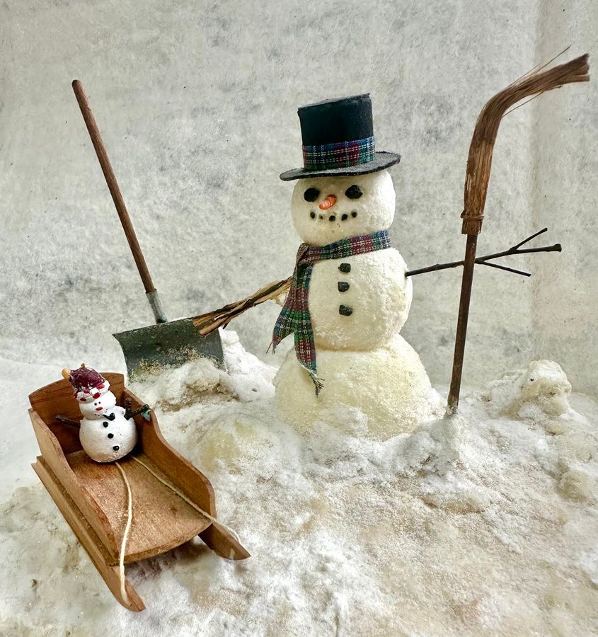 Snowmen in a snowy yard, one with a top hat and scarf, beside a small sled and shovel