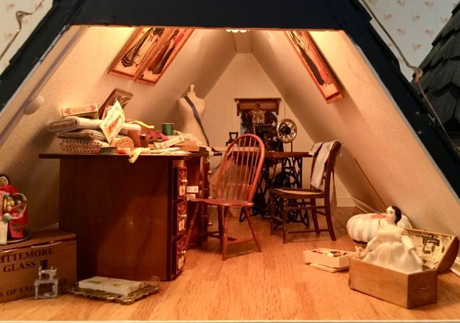 Cozy attic room with a desk, chairs, wooden floor, and a cat curled in a basket by the wall.