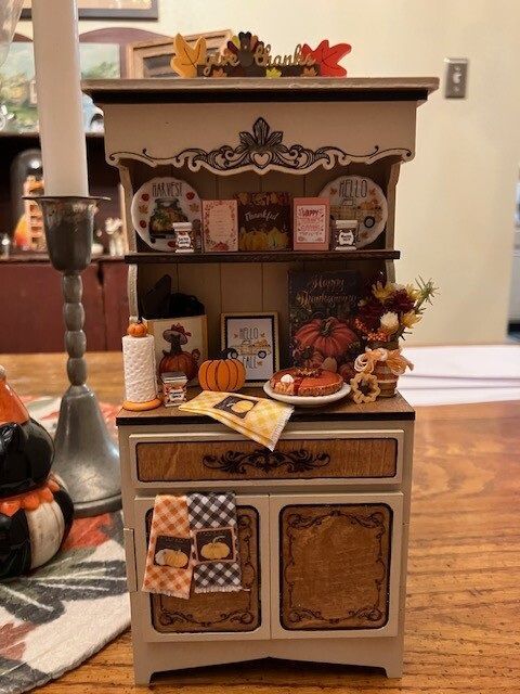 Miniature Halloween-themed hutch with pumpkins, candles, and autumn decorations indoors