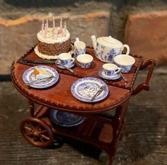 Miniature tea set on a wooden cart, with cake, teapot, cups, and plates on a rustic tabletop.