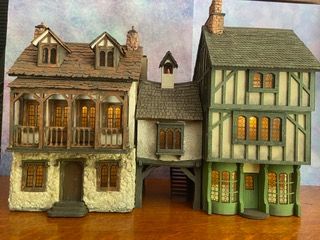 Three detailed miniature houses with ornate facades and warm-lit windows against a painted backdrop.