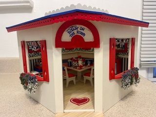 Tiny white-and-red miniature house with heart decor and open doors, showing a decorated interior.