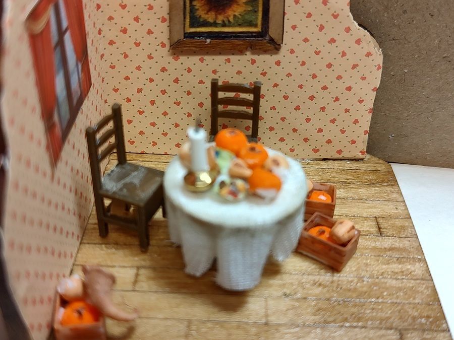 Miniature dining room with orange cats around a round table, chairs, and a wooden floor and wallpaper.