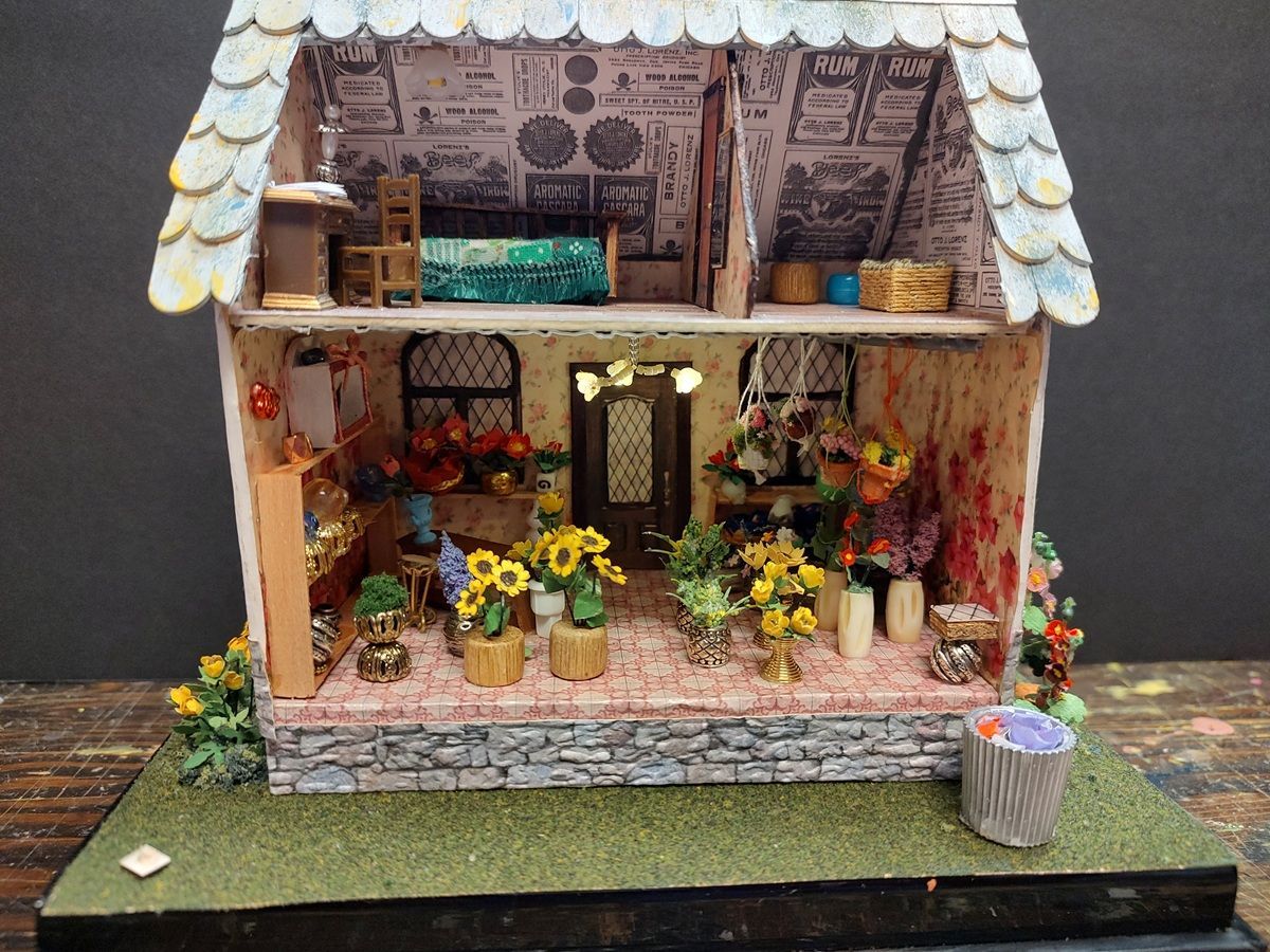 Miniature rustic flower shop dollhouse with a porch, yellow flowers, and a stone facade