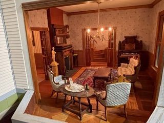Warm living room with hardwood floors, fireplace, chandelier, patterned rug, and vintage furniture