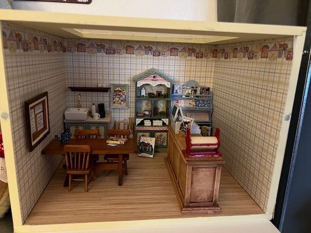 Miniature dollhouse room with a table, chairs, cabinet, and shelves against tiled walls