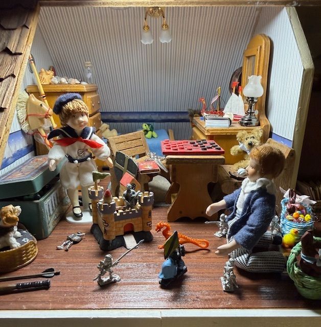 Miniature dollhouse room with toy figures, a table, shelves, and scattered small objects on a wooden floor