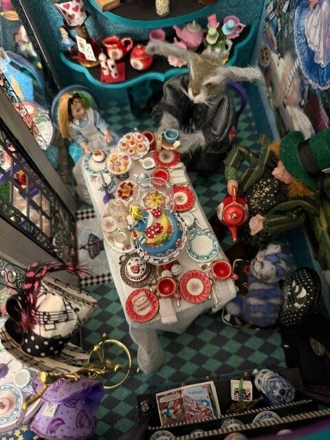 Miniature tea party scene with colorful tableware, dolls, and a cat on a patterned floor
