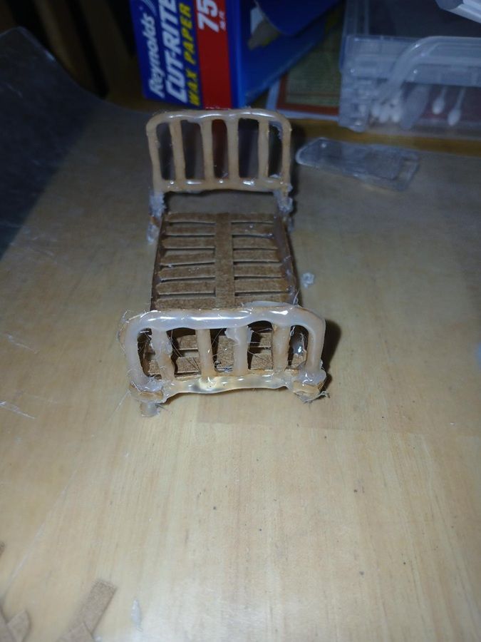 Rusty miniature metal bed on a wooden table, with a blue can and plastic container in the background