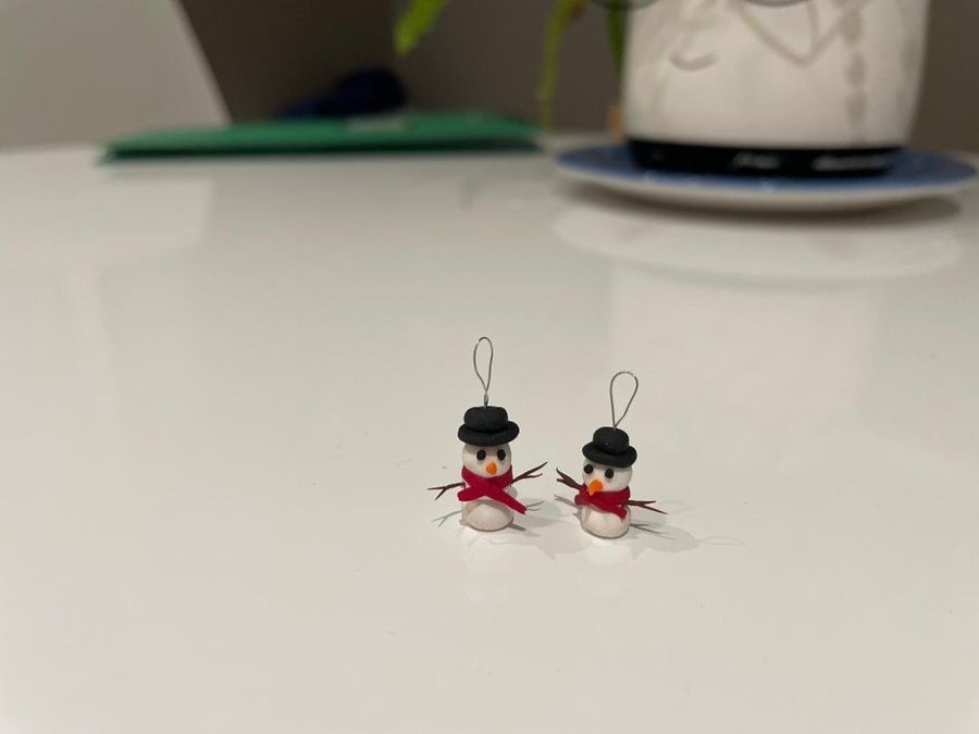 Two tiny red-and-black figurines with wire loops on a white tabletop, blurred mug in background