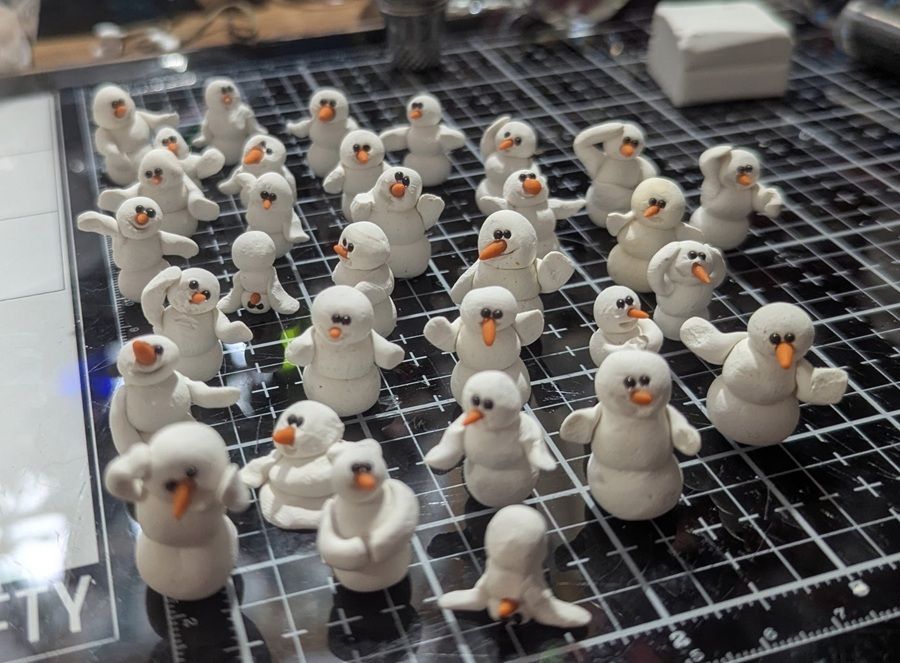 Many small white snowman figurines with orange noses on a cutting mat