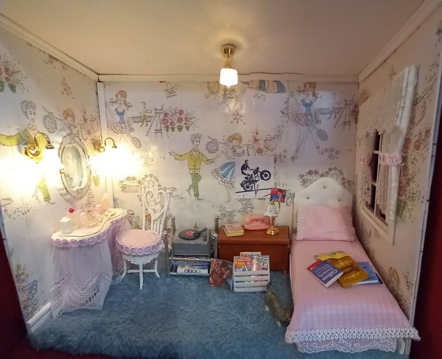 Child’s bedroom with floral wallpaper, pink bed, desk, stool, and blue carpet under a ceiling light
