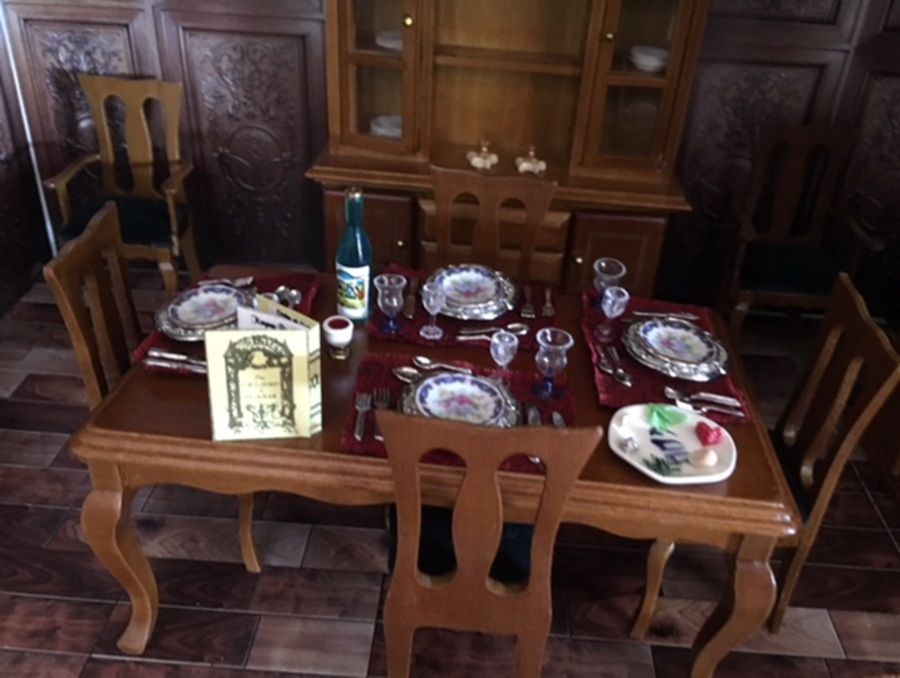 Set dining table in a wood-paneled room with plates, glasses, bottles, and chairs around it
