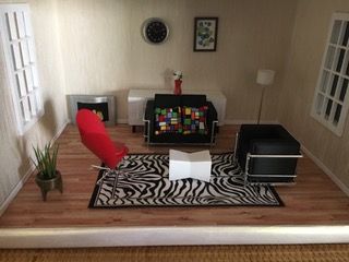 Modern dollhouse living room with red chair, zebra rug, black sofa, and small white coffee table