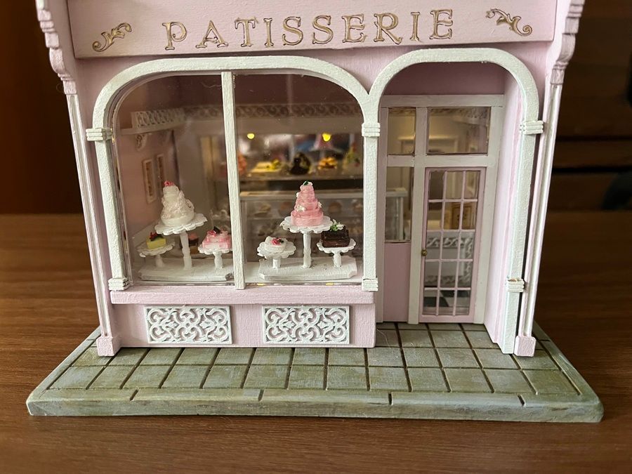 Pink miniature patisserie storefront with pastry display in the window and a tiled sidewalk.