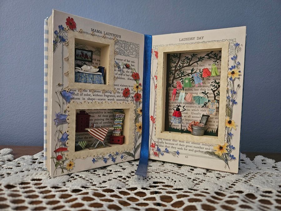 Decorative open book display with floral borders and two small framed photos on a lace tablecloth
