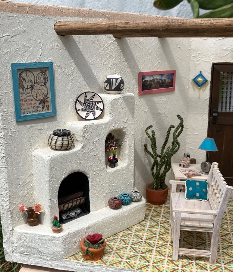 Miniature patio scene with white stucco fireplace, cactus, blue chairs, patterned tile floor, and wall decor