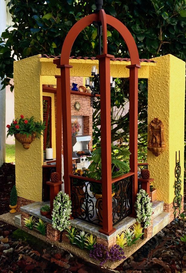 Decorative garden shrine with yellow walls, arched wooden frame, and potted flowers in a small courtyard