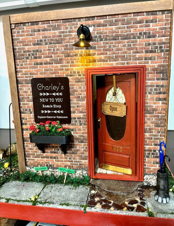 Small brick storefront with red door, chalkboard sign, flower box, and warm porch light.