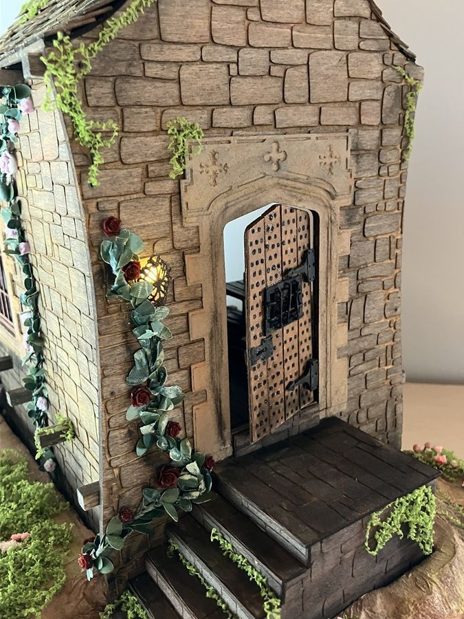Small stone house model with a dark door, wooden steps, and ivy growing up the side.