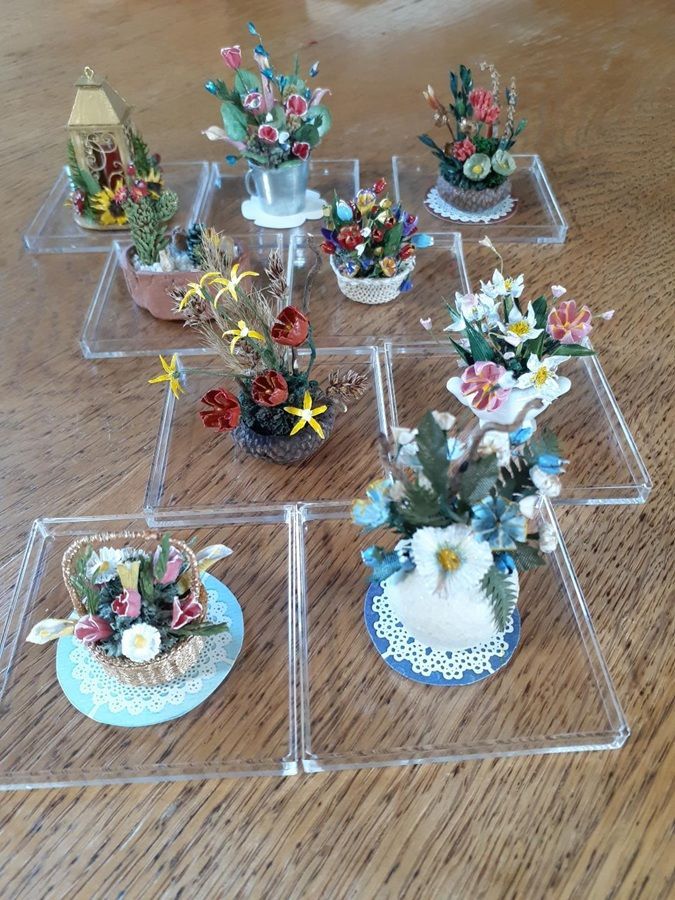 Miniature floral arrangements in small clear cases on a wooden table, with colorful flowers and a tiny vase centerpiece