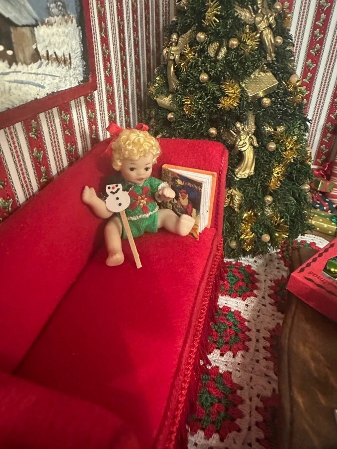 Red couch with dolls beside a lit Christmas tree and holiday decor