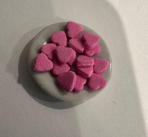 Pink heart-shaped candies in a small clear container on a white surface
