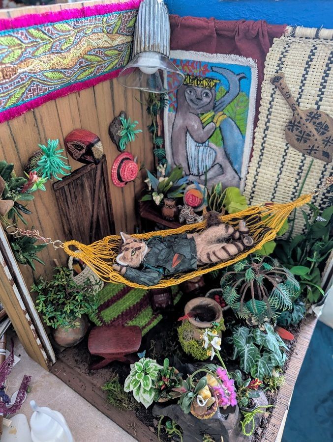 Miniature jungle diorama with a hammock, carved figures, lush plants, and colorful woven walls