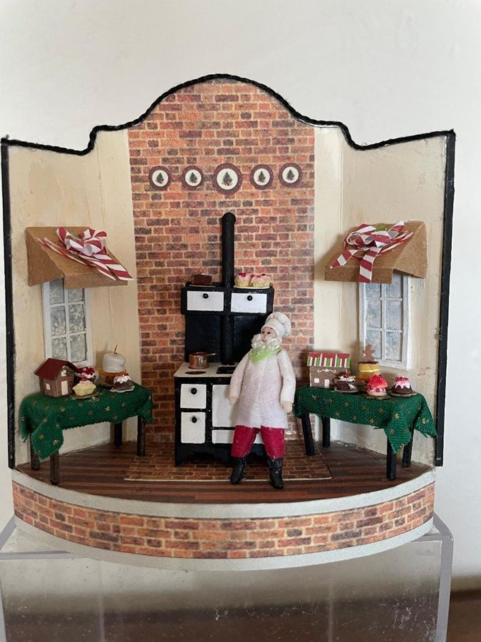Miniature room with brick fireplace, shelves, and a small doll standing on a wooden floor.