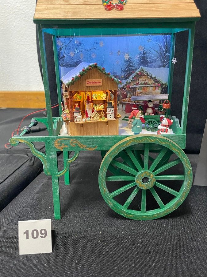 Miniature green cart with a lit holiday market display and large wheel, tagged 109
